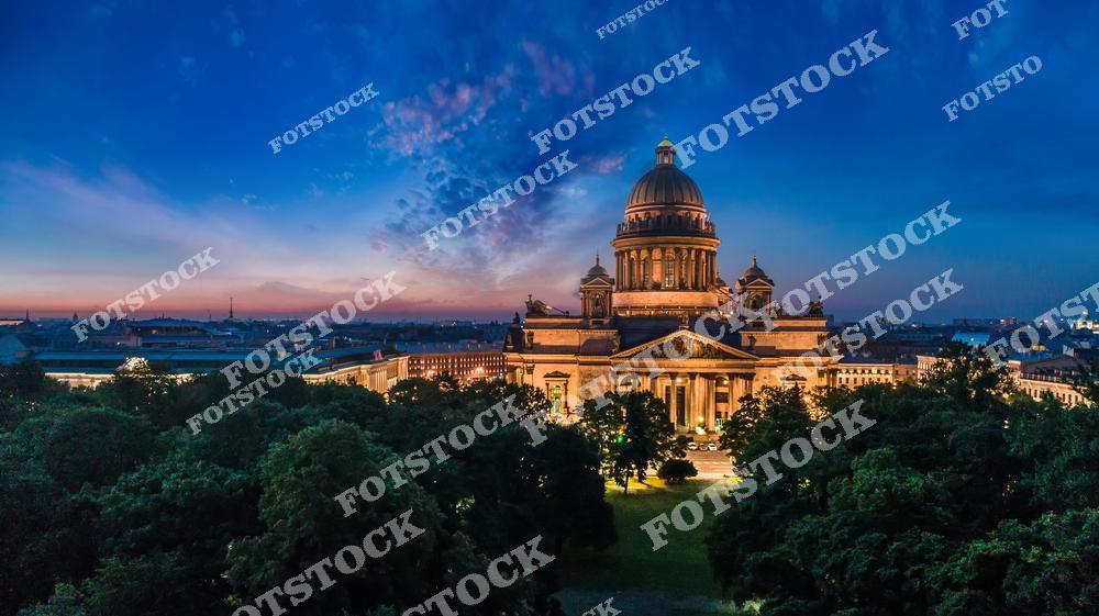 Панорамная фотография вечернего Санкт-Петербурга с высоты птичьего полета. На снимке запечатлен Исаакиевский собор, Невский проспект и исторический центр Северной столицы России в огнях вечернего города. Атмосферный вид с дрона передает архитектуру старого Петербурга, широкие улицы, знаменитые достопримечательности и уникальную городскую панораму. Фотография отлично подойдет для туристических проектов, рекламы, оформления интерьеров, публикаций о путешествиях и покупки изображений Санкт-Петербурга. Высотный ракурс позволяет увидеть красоту вечернего Питера, купола Исаакиевского собора и масштаб исторического центра города.